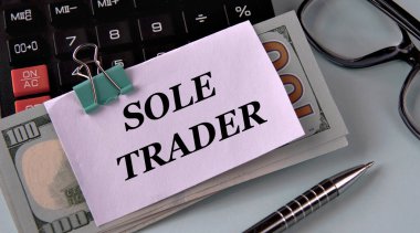 SOLE TRADER - banknotlara sabitlenmiş beyaz bir kağıt parçası üzerinde kelimeler bir hesap makinesi, gözlük ve kalem. İş ve finans kavramı