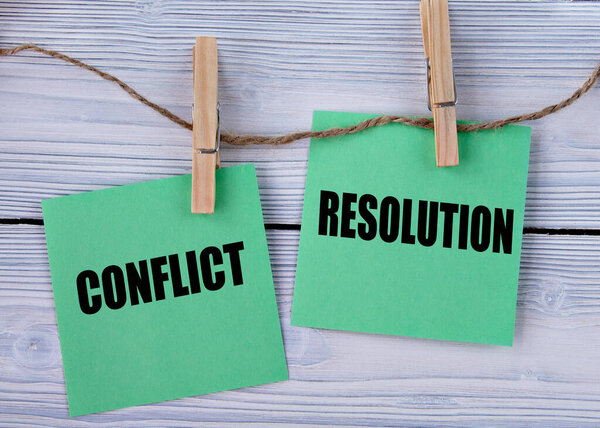 CONFLICT and RESOLUTION - words on green pieces of paper with clothespins on a light wooden background. Info concept