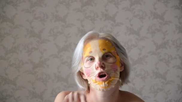 戴着化妆品面具的白人女人拿着耳机跳舞 戴着老虎面具的女孩在鬼混 玩得很开心 一个人呆在家里 — 图库视频影像