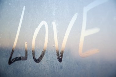 Aşk şehrin arka planındaki sisli pencereye çizilmiş. Sis camında parmak izi olan bir yazı aşkı. Sevgililer Günü tatili için tebrik kartı. Pencerede çizilmiş aşk.