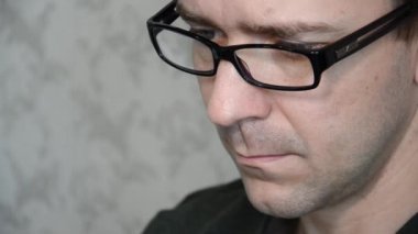 Caucasian man with glasses is working hard or studying. Portrait of young man looking at device in his hands. The concept of work or study online.