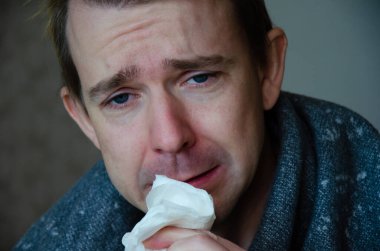 Battaniyenin altındaki hasta beyaz adam peçeteleri kokluyor. Adamın soğuk, hasta bakışları ve akan burnu var. Hastalık sezonu konsepti.