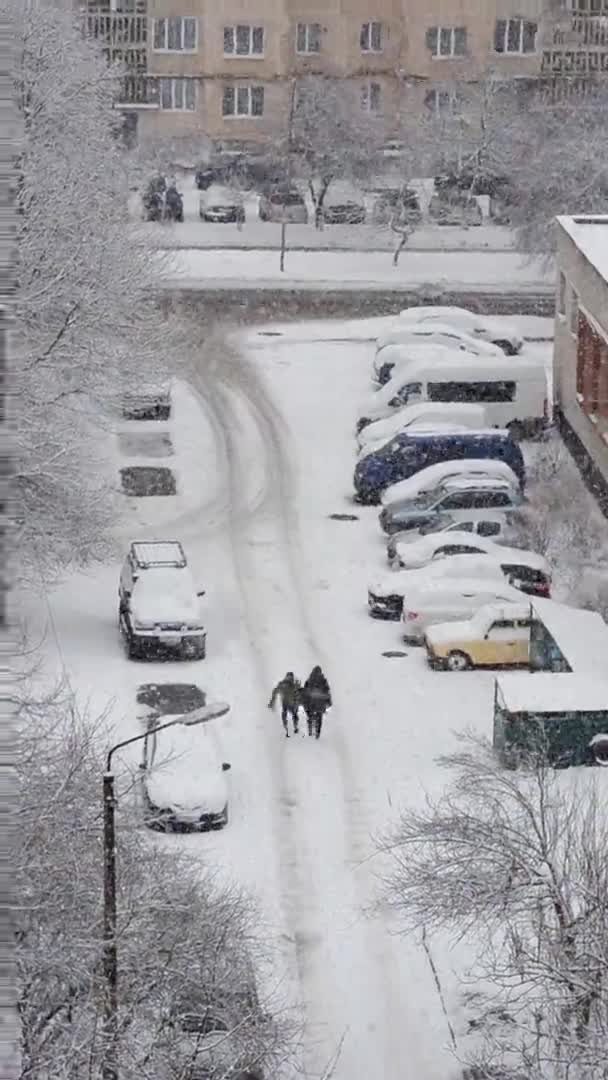 人们在白雪覆盖的房子和汽车中间走着 城市的冬季天气 雪崩了暴雪覆盖了整个城市 垂直镜头 — 图库视频影像