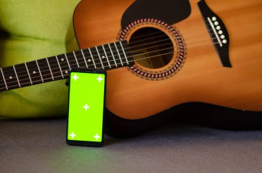 Gitarın yanında kopyalama alanı olan işaretleyici işaretleri olan yeşil ekran kromakey modelli telefona odaklan. Yeşil ekran ve krom anahtar. Çevrimiçi gitar dersleri.