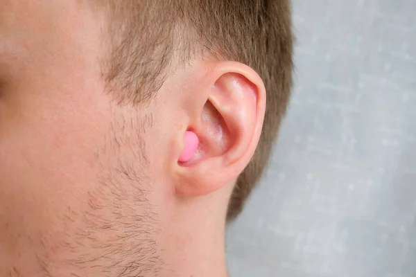A pink wax earplug is inserted into the ear.