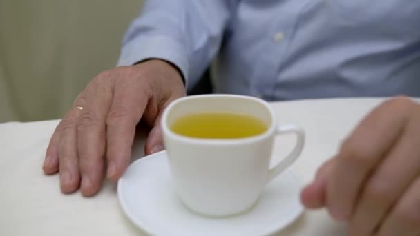 Close-up shot of a mans hand in a blue shirt with a cup of tea — Stock Video