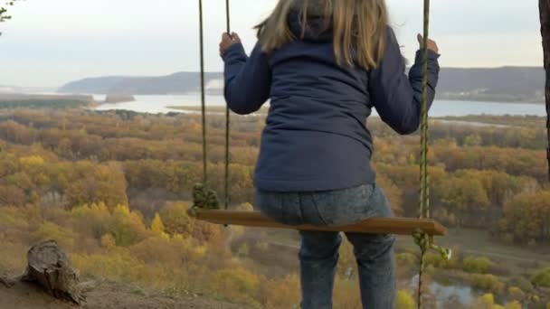 少女は標高の高いところでスイングに乗っている。自然の中で山の上でスイング。丘の上の春休み — ストック動画