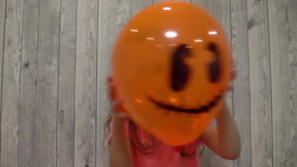 La fille se cache derrière un ballon avec un visage effrayant peint. Célébrons Halloween. Boule sous la forme d'une citrouille effrayante — Video