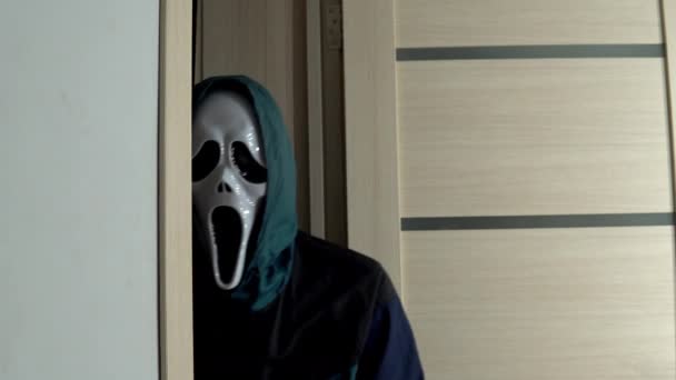 Egy ismeretlen ember jelenik meg sikoltozó maszkban az ajtóban. Egy mániákus ijesztő maszkban téged néz. A maszk másolata a Sikoly című filmből. Halloween ünnepe — Stock videók