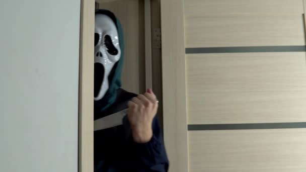 Una persona desconocida con una máscara de gritar con un cuchillo en la mano emerge de la puerta. Maniaco con una máscara de miedo. Una copia de la máscara de la película Scream. Halloween celebración — Vídeos de Stock