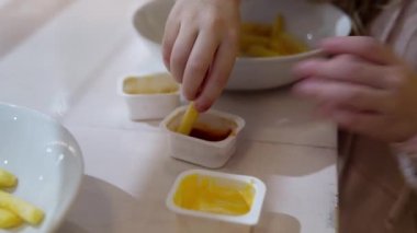 Restoranda küçük bir kız soslu patates kızartması yiyor. Çocuk enstitüde yemek yiyor. Patatesleri sosa bandırın.
