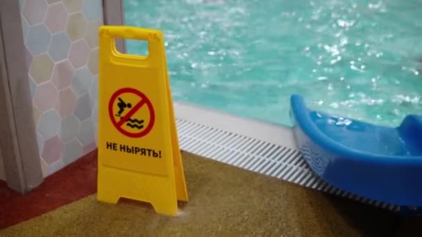 A inscrição em russo não mergulha. Um sinal amarelo fica perto da piscina com uma inscrição de advertência contra o fundo das pessoas que flutuam na piscina — Vídeo de Stock