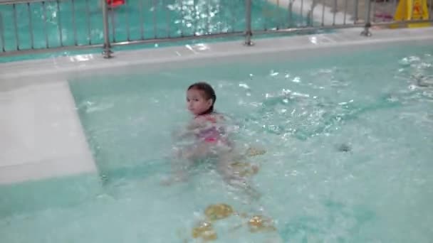 Ein kleines Mädchen mit nassen Haaren im rosafarbenen Badeanzug schwimmt im Pool des Wasserparks — Stockvideo