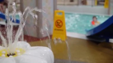Su parkındaki çocuk çeşmesi havuzda banyo yapan insanların arka planına karşı çiçek şeklinde.