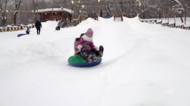 Anne ve kızı bir hovercraftta kar kaydırağından aşağı kayıyorlar. Aileyle birlikte kış parkında buz kayakları.