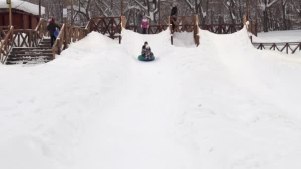 Mamá y su hija viajando por un tobogán de nieve en un aerodeslizador. Toboganes de hielo en un parque de invierno con la familia — Vídeo de stock