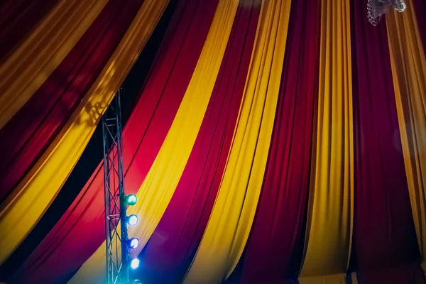 Ceiling decorated with heavy fabrics and light bulbs to show a circus feeling. Colorful curtain and light bulb decorations. Circus party decorations. Circus tent from inside.