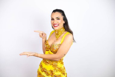 Karnaval kostümü giyen genç ve güzel bir kadın izole edilmiş beyaz arka planda şaşırmış ve elindeki bir şeyi gösteriyor.