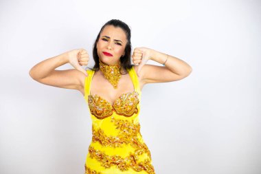 Karnaval kostümü giyen genç güzel bir kadın izole edilmiş beyaz arka planda kızgın yüzlü, negatif işaretli baş parmakları aşağıda hoşnutsuzluk gösteriyor.