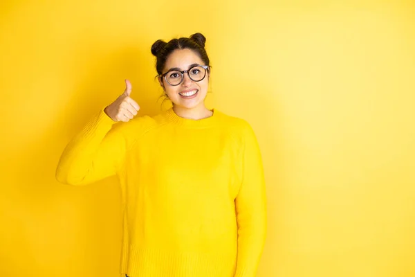 孤立した黄色の背景の成功の印の上にカジュアルなセーターを身に着けている若い美しい女性は 手で積極的なジェスチャーを行い 親指を笑顔と幸せ 陽気な表情 — ストック写真