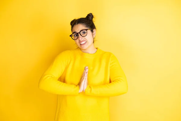 Young beautiful woman wearing casual sweater over isolated yellow background begging and praying with hands together with hope expression on face very emotional and worried