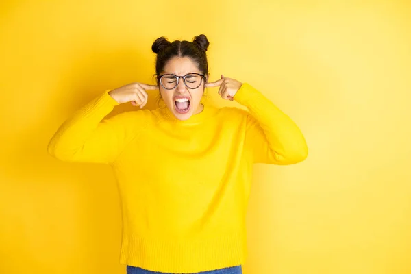 無声音楽のノイズに悩まされる表情で指で耳を覆う孤立した黄色の背景にカジュアルなセーターを着た若い美しい女性 ろう者の概念 — ストック写真