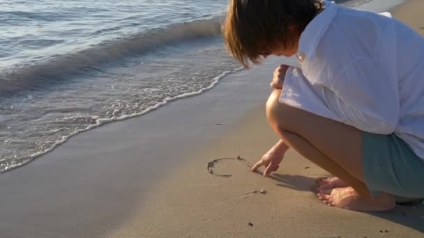 Frau zeichnet bei Sonnenuntergang ein Herz auf den Sand — Stockvideo