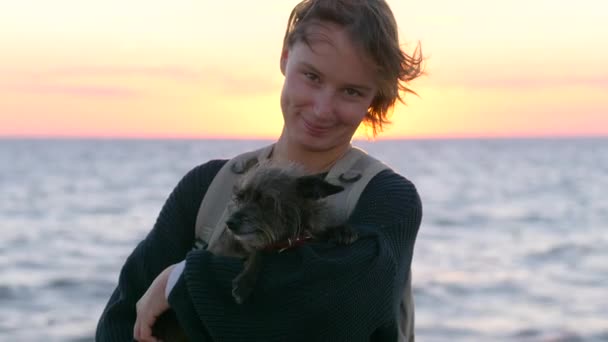 Frau hält ihren süßen Hund vor dem Meer bei Sonnenuntergang — Stockvideo