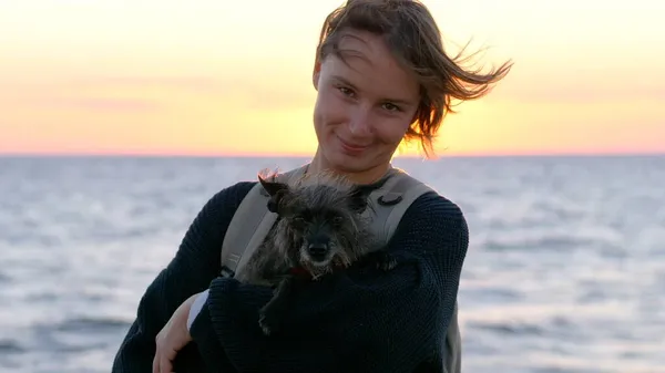 Женщина, держащая свою милую собаку перед морем на закате — стоковое фото