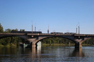 Vltava Nehri üzerindeki köprüdeki tramvaylar Zhizhkov TV kulesinin (ikovsk vysla) arka planına ve yeşil ağaçlara ve mavi yaz gökyüzüne karşı