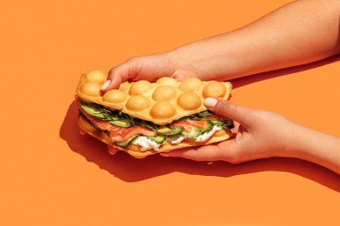 Somon, roka, marul, krem peynir ve turuncu arka planda izole edilmiş salatalıklı waffle sandviçi. Fast food, götür. Atıştırmalık