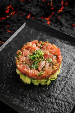 Çiğ ton balığı, avokado soğan salatası ve siyah tabakta servis edilen yemek halkası. Siyah arka plan. Tatar.