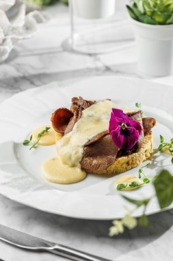 Açık mermer arka planda, beyaz tabakta krema soslu pirinç garnitürlü dilimlenmiş sığır eti. Sağlıklı deniz ürünleri, sert ışık, restoran dekorasyonu, yakın çekim.