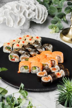 Philadelphia 'lı taze suşi seti. Japon deniz ürünleri suşisi açık mermer arka plandaki siyah tabakta. Sağlıklı deniz ürünleri, sert ışık, restoran dekorasyonu, yakın çekim.