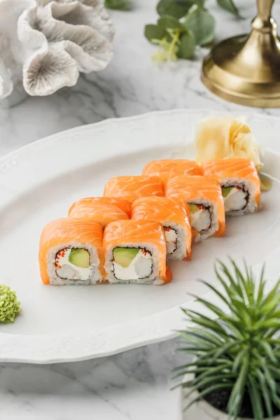 Closeup image of classic philadelphia sushi rolls with salmon, cheese and cucumber in the white plate on light marble background. Healthy sea food, hard light, restaurant decor