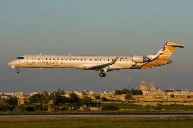 Luqa, Malta - 4 Eylül 2010: Libya Hava Yolları Bombacısı CRJ-900ER (CL-600-2D24) (REG: 5A-LAA) iniş pisti 31, batan güneşin sıcak ışığıyla aydınlandı. 