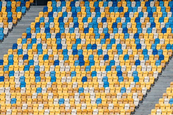 Blurred sitting fans colored plastic chairs at the football stadium background. Closeup of yellow and blue seats on stadium. ArenaLviv Ukraine.