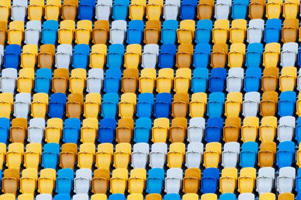Размытые сидящие вентиляторы окрашивали пластиковые стулья на заднем плане футбольного стадиона. Крупный план жёлтых и синих сидений на стадионе. ArenaLviv Украина.