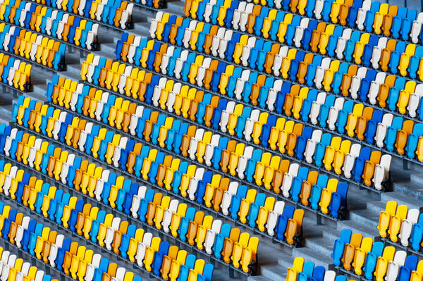 Blurred sitting fans colored plastic chairs at the football stadium background. Closeup of yellow and blue seats on stadium. ArenaLviv Ukraine.