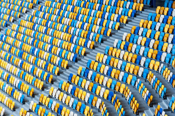 Blurred sitting fans colored plastic chairs at the football stadium background. Closeup of yellow and blue seats on stadium. ArenaLviv Ukraine.