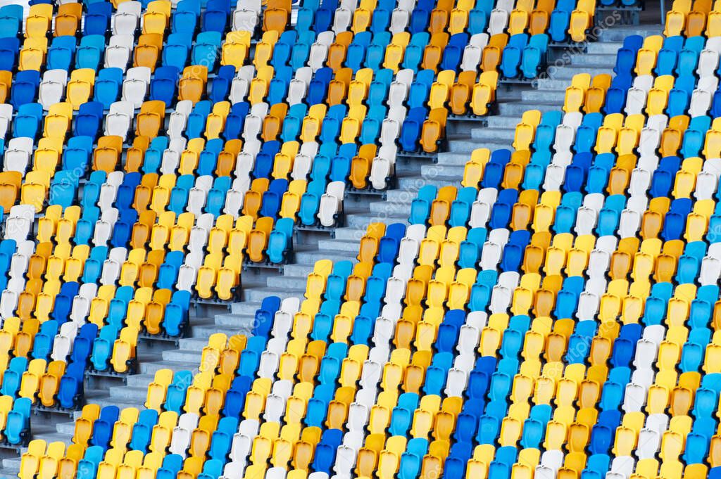 Blurred sitting fans colored plastic chairs at the football stadium background. Closeup of yellow and blue seats on stadium. ArenaLviv Ukraine.