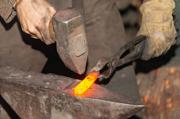 Blacksmith working metal with hammer on the anvil in the forge