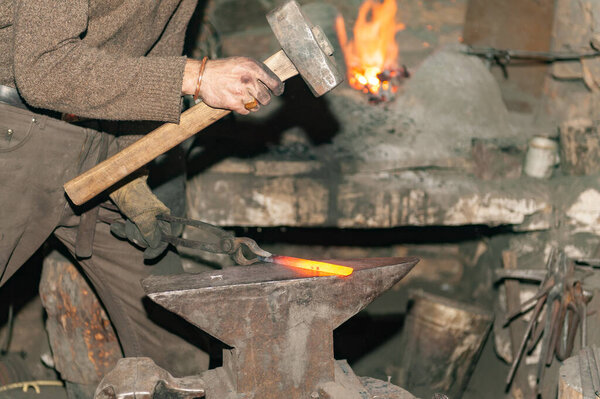 Blacksmith working metal with hammer on the anvil in the forge