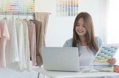 Bir tasarımcının atölyesinde dizayn ekipmanı, dizüstü bilgisayarı ve akıllı telefonu olan genç bir kadın terzi..