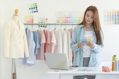 Bir tasarımcının atölyesinde dizayn ekipmanı, dizüstü bilgisayarı ve akıllı telefonu olan genç bir kadın terzi..