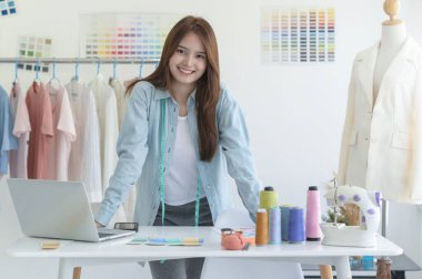 Bir tasarımcının atölyesinde dizayn ekipmanı, dizüstü bilgisayarı ve akıllı telefonu olan genç bir kadın terzi..