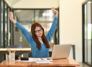 Mavi gömlekli Asyalı kadın rahatlamak için kollarını açıyor. Ofiste çalışırken, ofis sendromu, iş fikri, ofis ekipmanları....