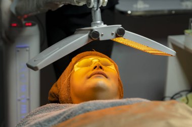 Gözleri bağlı ve radyasyonlu cilt bakımı, güzellik kliniğinde biyoışık terapisi, yüz gençleştirme için sarı ışık, güzellik kavramları..