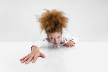 Beyaz arka planda izole bir şekilde oturan ve kameraya bakan güzel okul kızının yakın plan portresi..