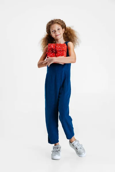 Ένα χαρούμενο χαριτωμένο καυκάσιο κοριτσάκι weraing μπλε κοστούμι στέκεται με τεράστιο δώρο, κουτί διακοπών απομονώνονται σε γκρι φόντο στούντιο με copyspace για διαφήμιση — Φωτογραφία Αρχείου
